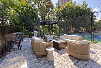 A patio with couches and tables and a tennis court in the background
